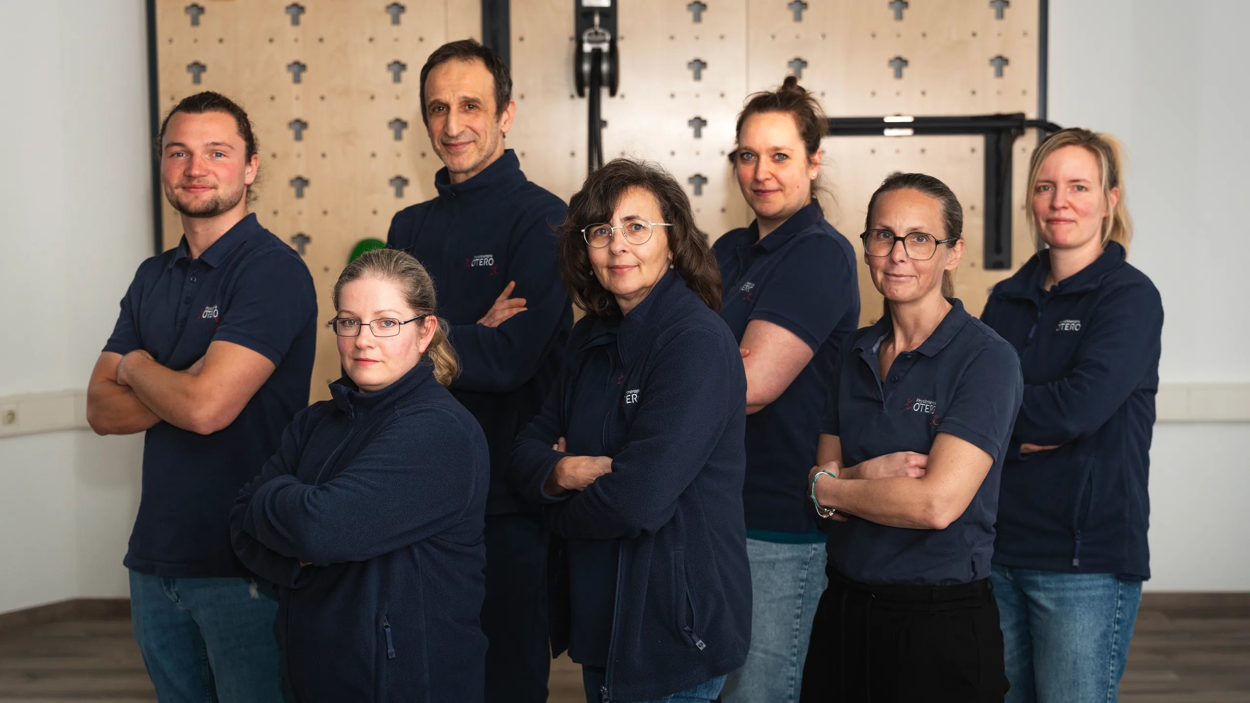 Das Team der Physiotherapie Otero im Trainingsraum vor der Birkenholz-Trainingswand